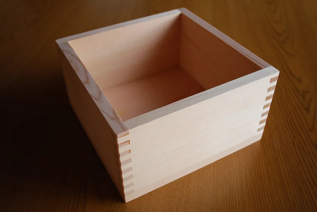 Un masu de verdad: caja cuadrada de madera con las esquinas ensambladas, vacía, sobre una mesa de madera